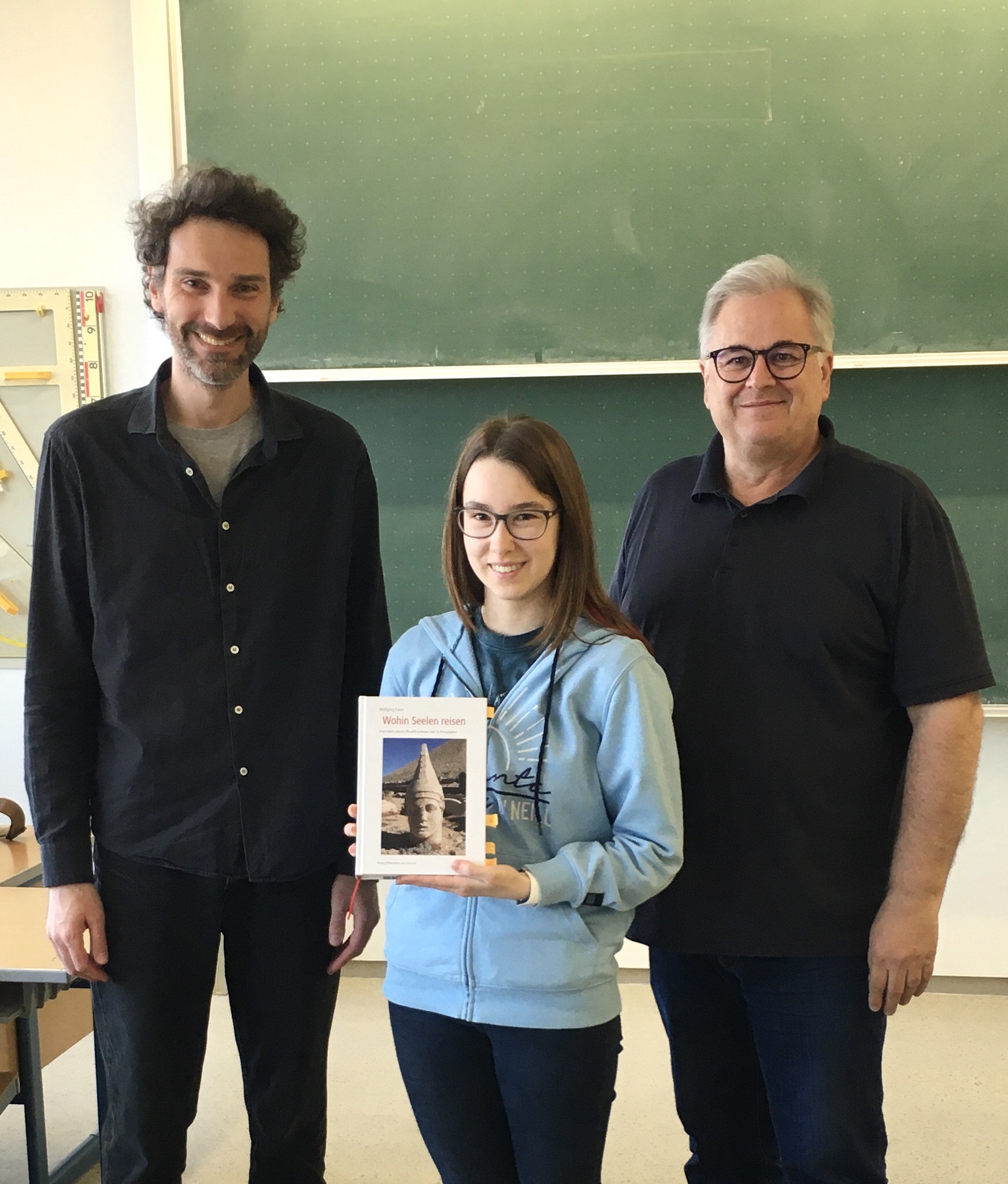 Schülerin Laura bekommt als Erste Wolfgang Kauers Buch „Wohin Seelen reisen. Inspirative Jenseits-Modelle weltweit und in Petroglyphen“, das nach jeder Lektüre weitergegeben werden soll. Projekt »Sternlesen«, Andorf Technology School, am 11.04.2025. Foto: Schüler Jakob. Abdruck/Veröffentlichung honorarfrei bei Namensnennung.