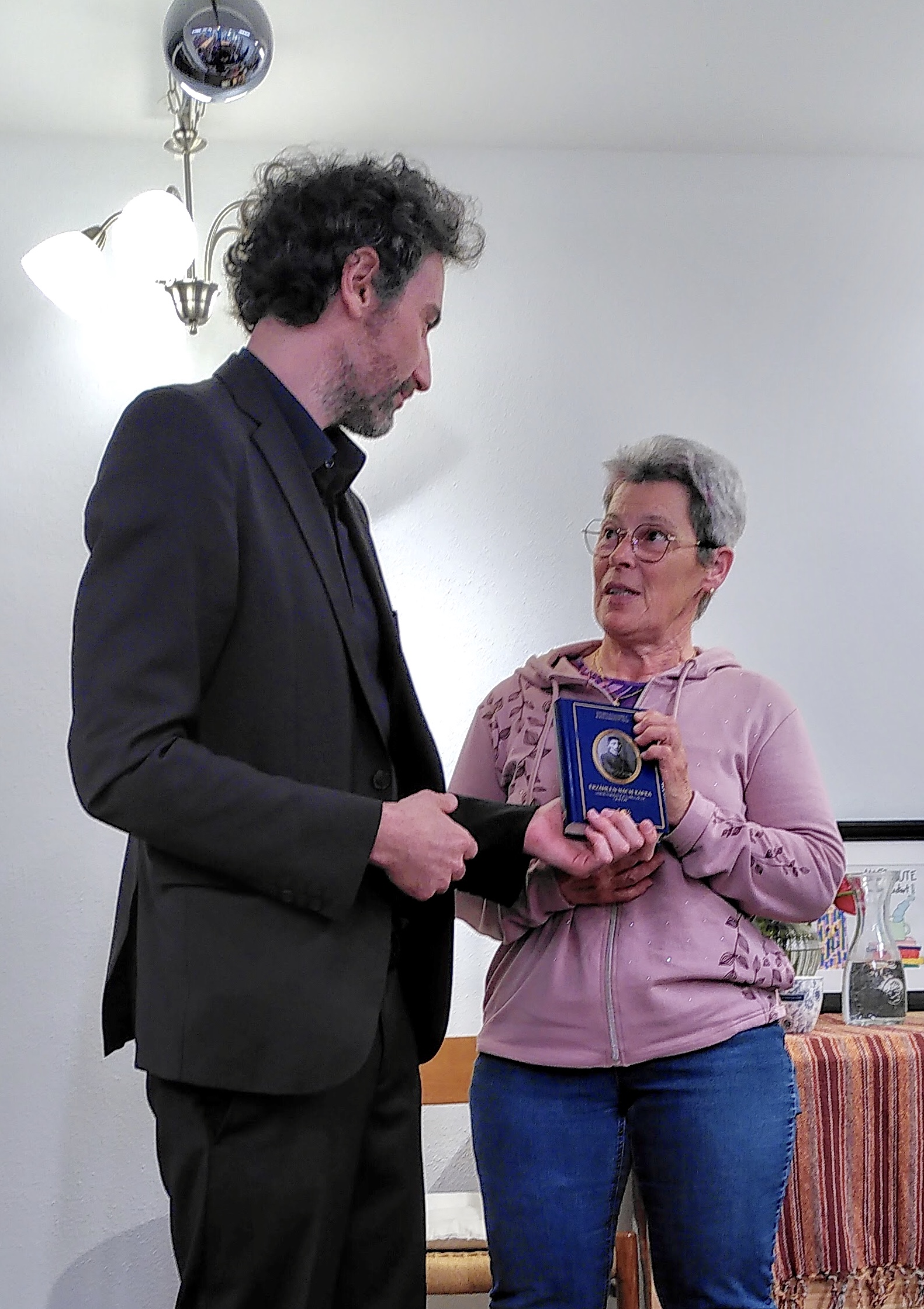 Stefan Reiser überreicht die Anthologie „Erzählen nach Kafka. Verwandlungen, Prozesse, Gesetze“ an eine Zuschauerin. Das Buch soll nach jeder Lektüre weitergegeben werden. Projekt »Sternlesen«, Buchhandlung Schachinger, Schärding, am 11.04.2025. Foto: Ulrike Schachinger. Abdruck/Veröffentlichung honorarfrei bei Namensnennung.