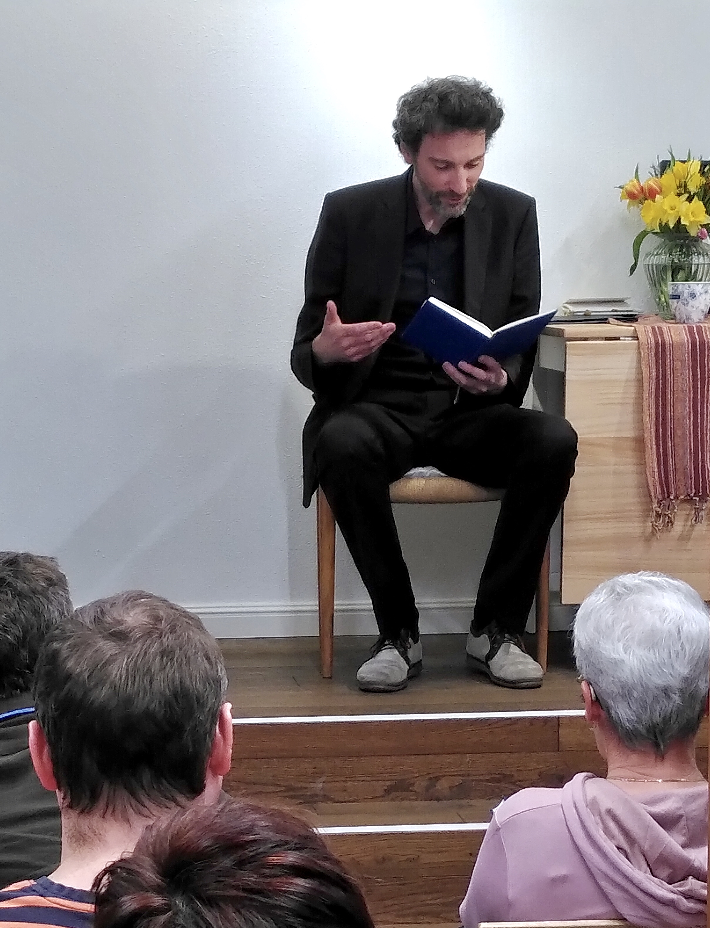 Stefan Reiser gestikuliert während seiner szenischen Lesung. Das Publikum lauscht. Projekt »Sternlesen«, Buchhandlung Schachinger, Schärding, am 11.04.2025. Foto: Ulrike Schachinger. Abdruck/Veröffentlichung honorarfrei bei Namensnennung.