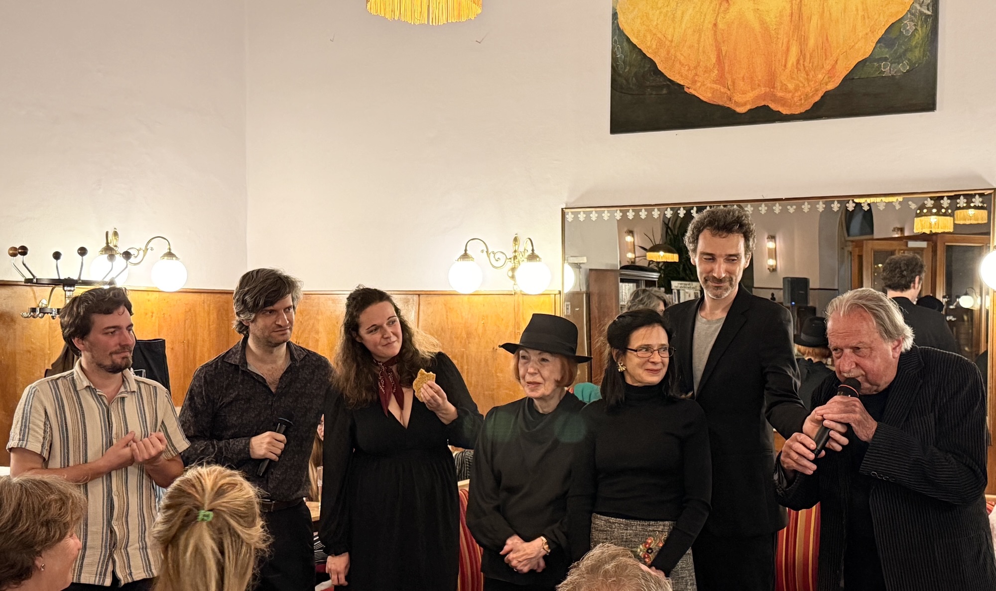 Von links nach rechts: Marius Binder (Klavier), Alexander Estis, Anna Fercher, Christl Greller, Marlen Schachinger-Pusiol, Stefan Reiser, Manfred Ach lesen MINUTENTEXTE. Organisation u. szenische Einrichtung: Reiser. Café Schopenhauer, Wien, am 16.09.2026. Foto: © Doris Sidl.